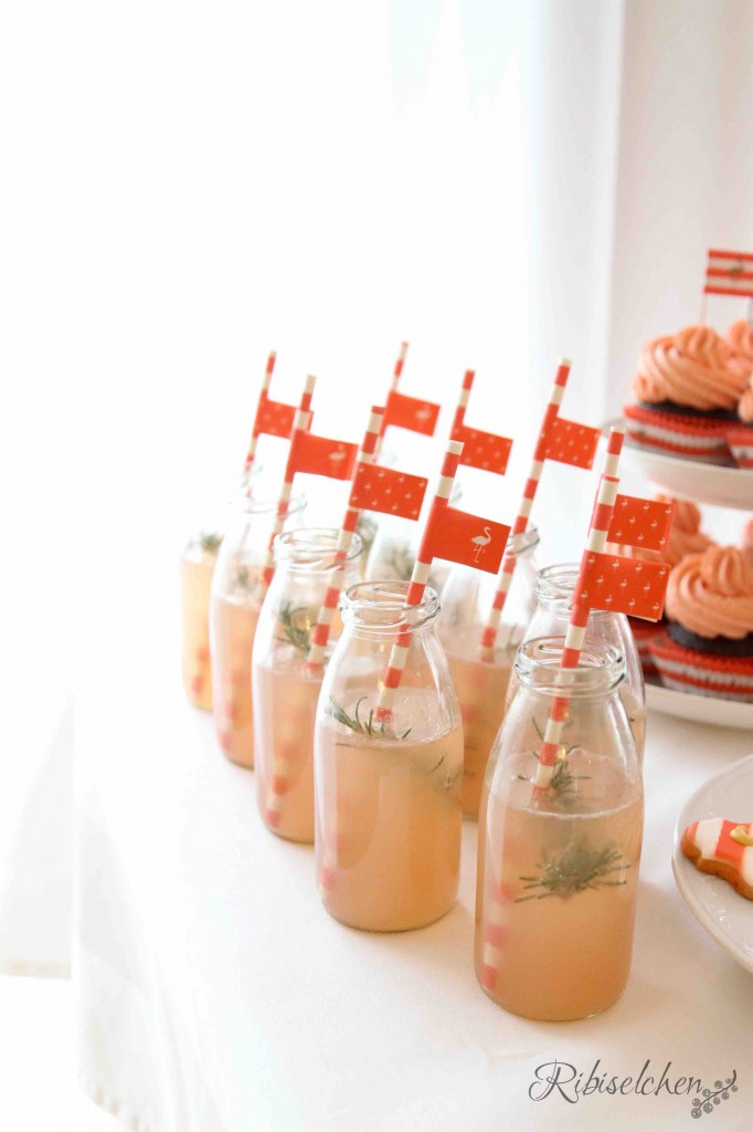 Mehrere kleine Glasflaschen mit Grapefruit-Rosmarin-Limonade und Strohhalmen mit Fähnchen