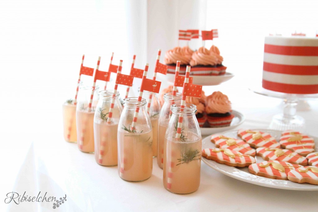 Blick auf den Sweet Table mit den Flaschen mit der Limonade im Vordergrund, im Hintergrund Cupcakes, Kekse und eine Torte.