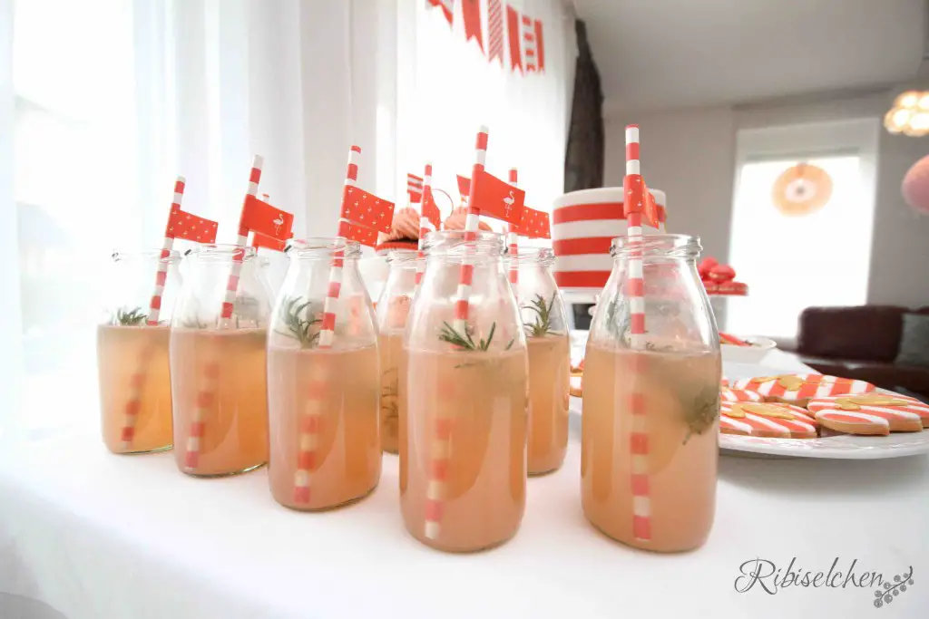 Mehrere kleine Glasflaschen von der Seite mit Grapefruit-Rosmarin-Limonade und Strohhalmen mit Fähnchen 
